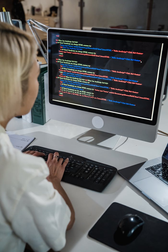 A female programmer writing code on a desktop computer in an office setting with a focus on technology and IT development.